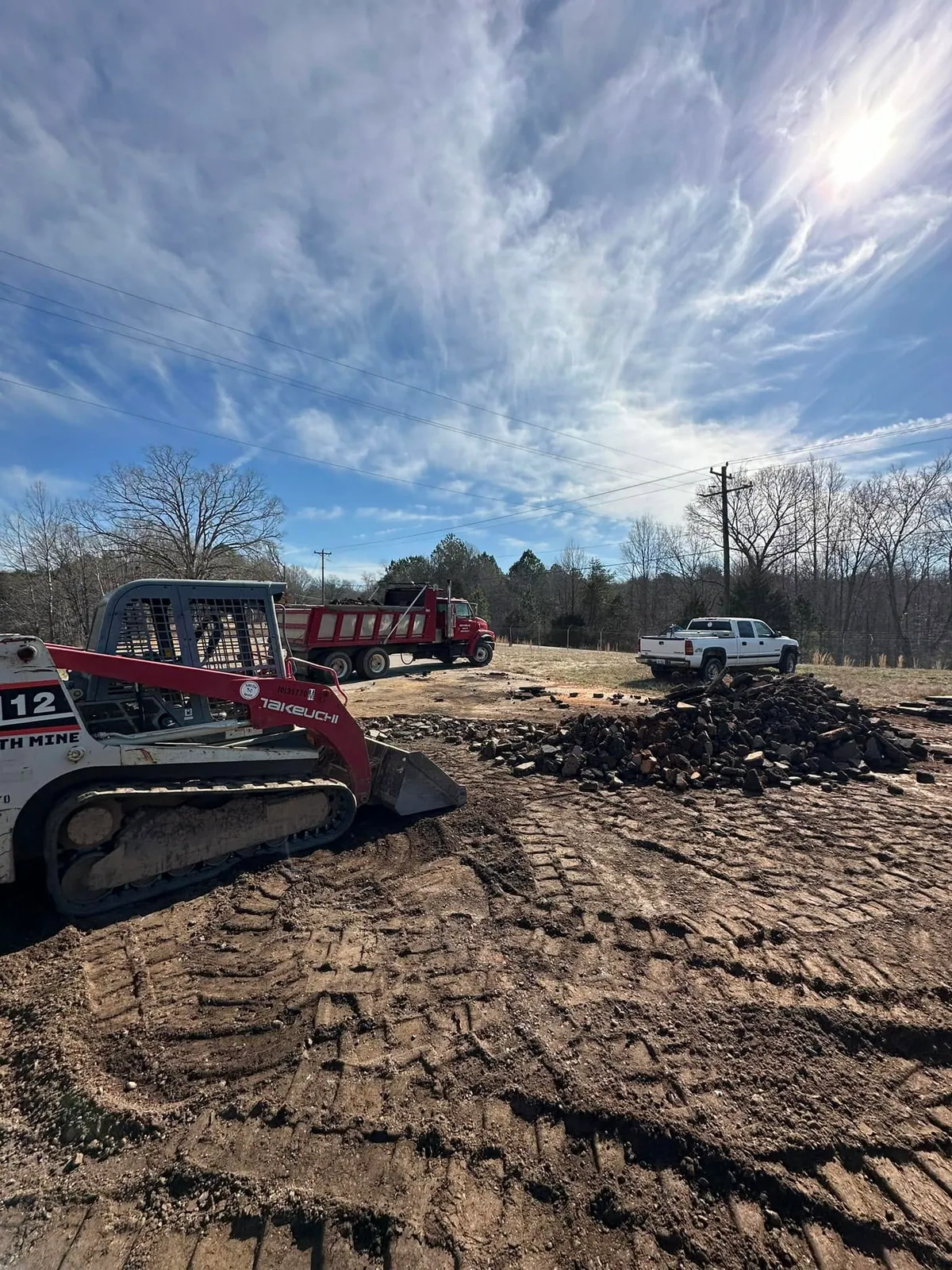 Takeuchi track loader tearing out asphalt parking lot, red tandem dump truck loaded with broken asphalt