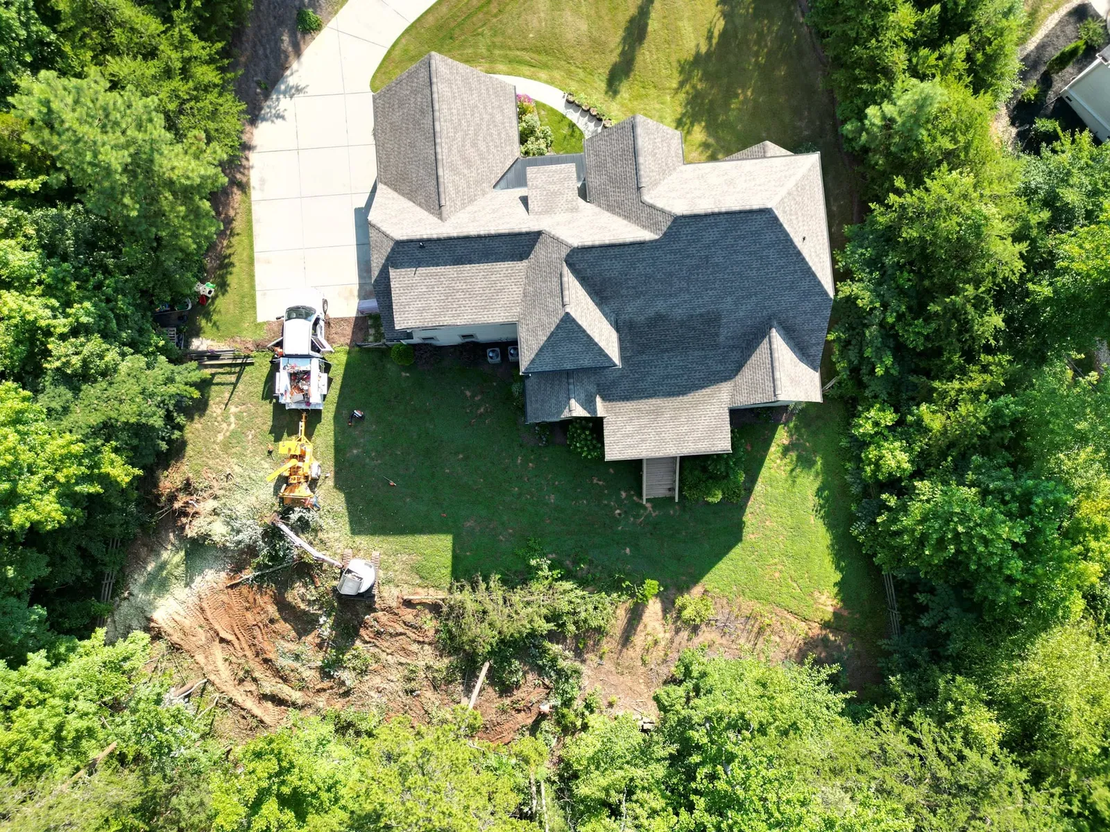 Drone view of large house; chipper truck, Bandit chipper and skid steer clearing brush along back tree line