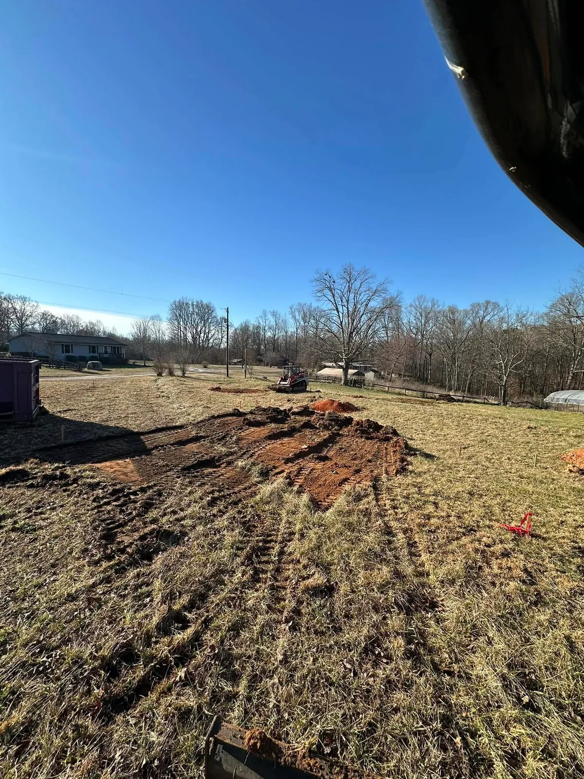 Cab view of topsoil stripping just starting on staked field pad; Takeuchi track loader and dumpster nearby