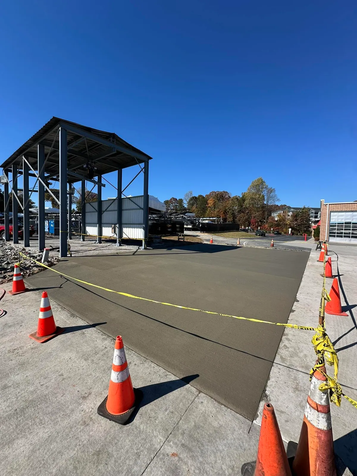 Cured new concrete slab under steel canopy with cones and caution tape at boat dealership