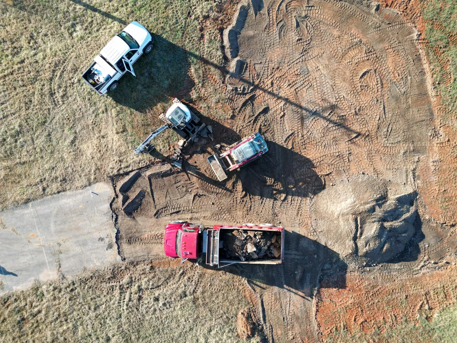 Drone aerial: Bobcat mini excavator, Takeuchi track loader and red dump truck breaking out old concrete slab