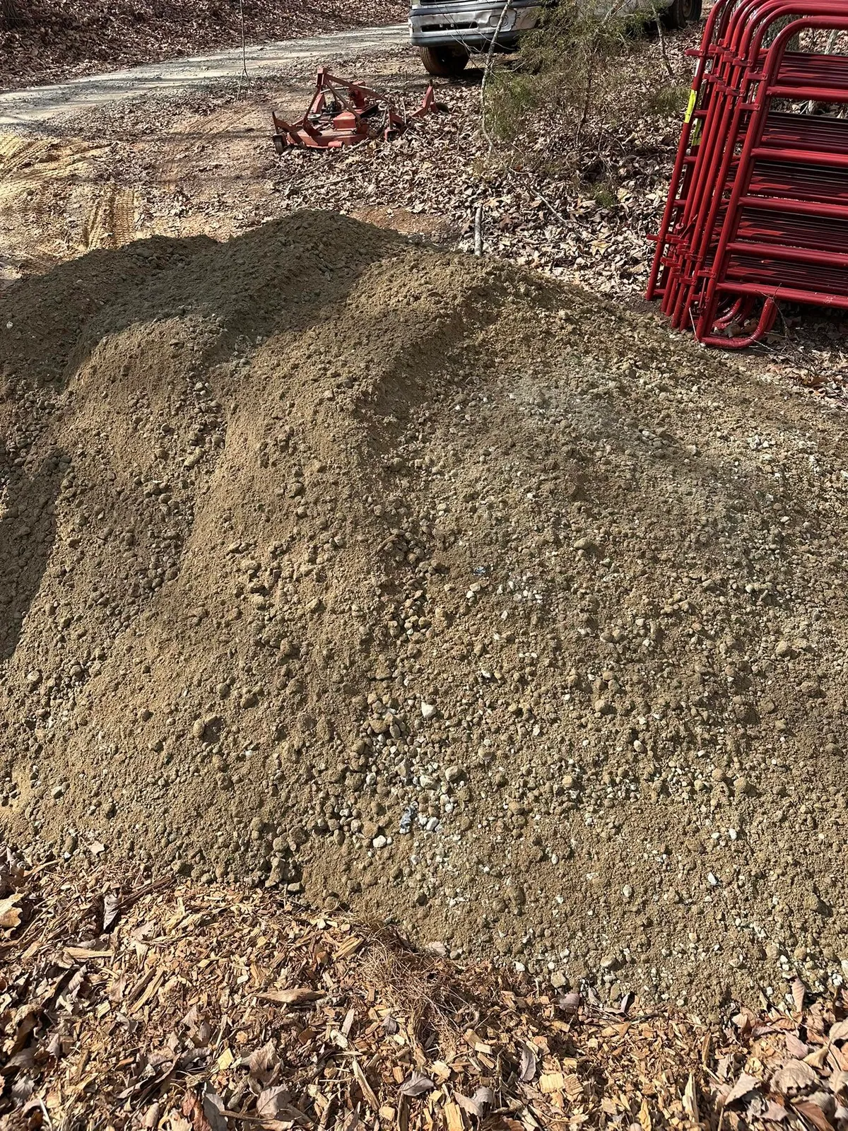 Pile of crushed concrete aggregate dumped beside gravel drive, red livestock panels and bush hog nearby