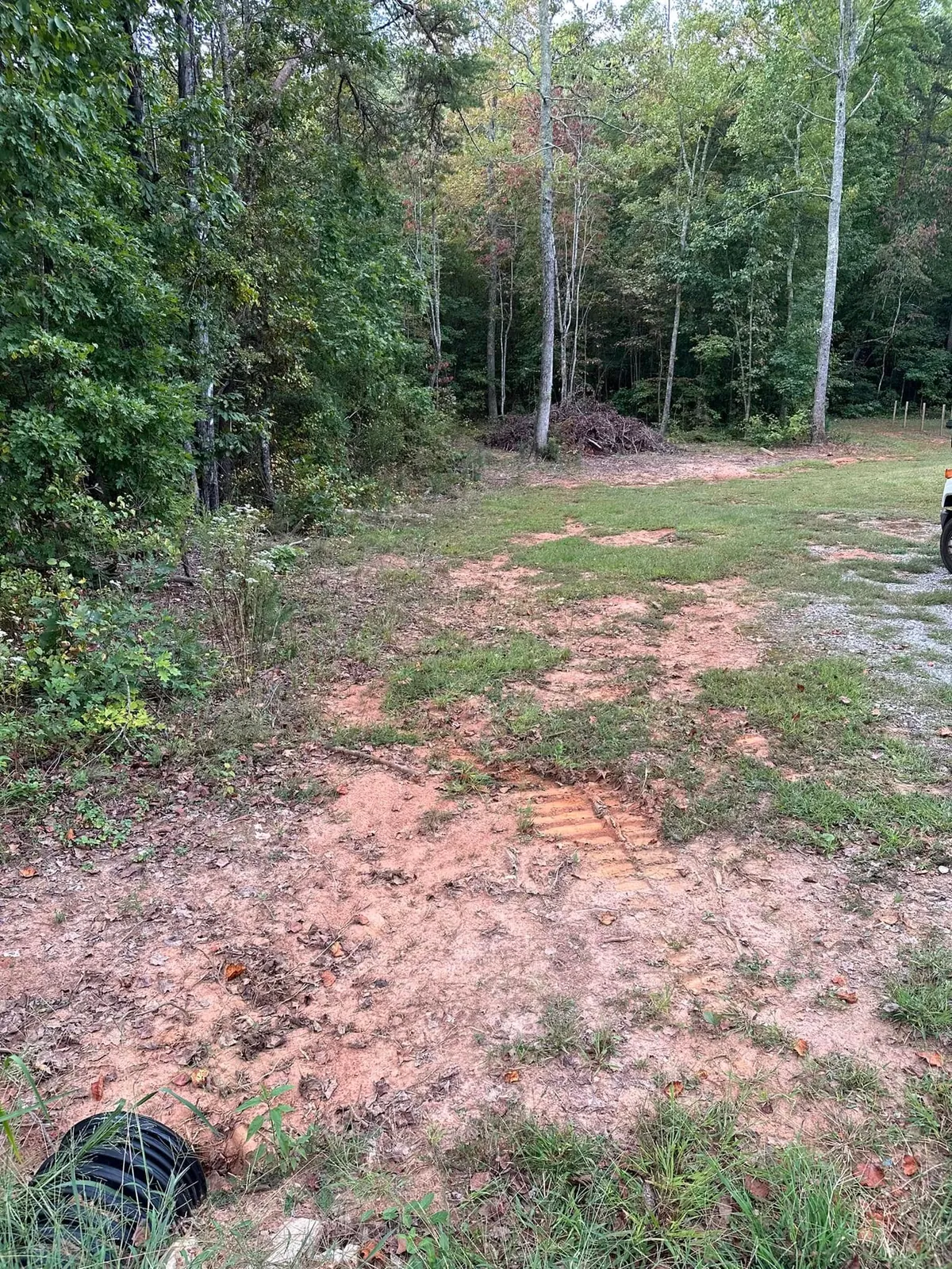 Overgrown lot edge with black corrugated culvert pipe lying in grass before ditch and driveway work