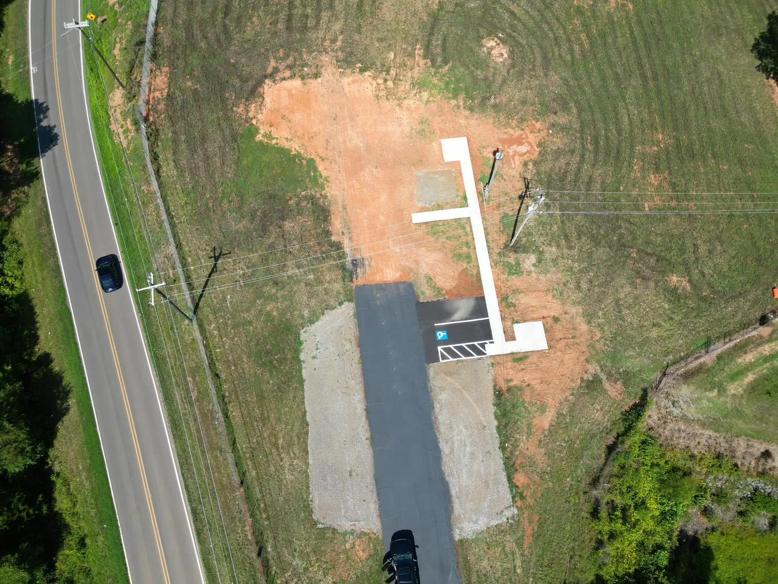 Drone view of finished dog park phase 1: asphalt parking strip, gravel shoulders, ADA sidewalk, graded field in Maiden, NC