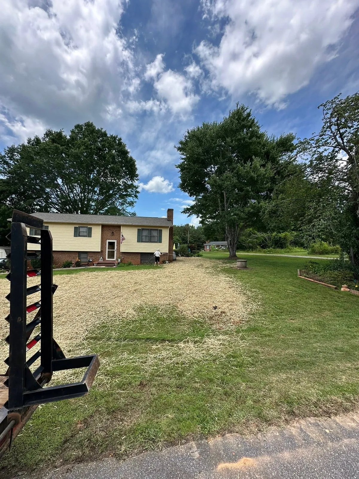 Front yard regraded and strawed after drain line install, homeowner watering, trailer ramp in foreground