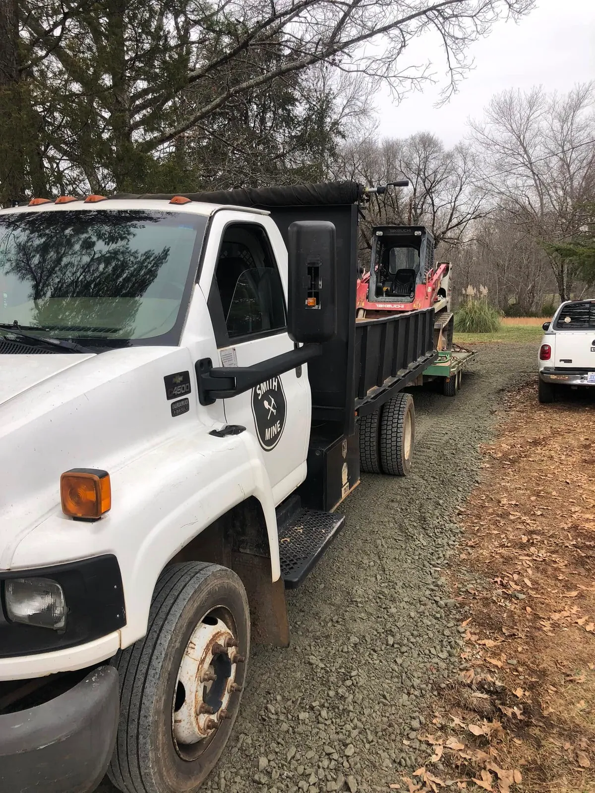 Smith Mine Chevy C4500 Duramax dump truck towing red Takeuchi track loader on fresh gravel driveway