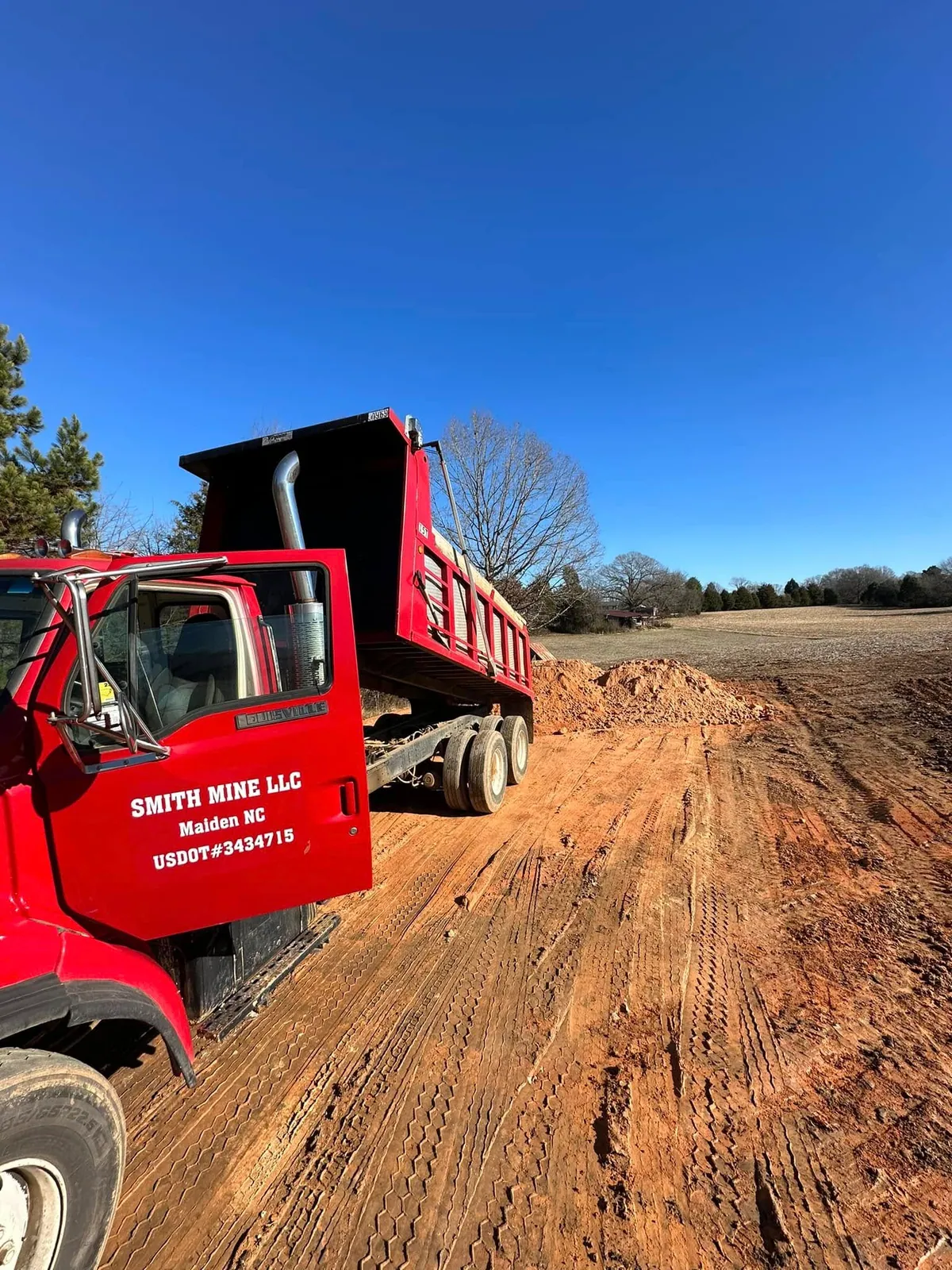 Smith Mine red Louisville dump truck dumping fill dirt pile on open farm field under clear blue sky