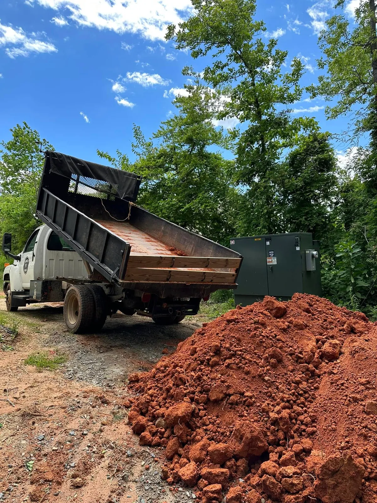 Smith Mine Chevy C4500 dump truck bed raised after dumping red clay fill beside pad-mount transformer