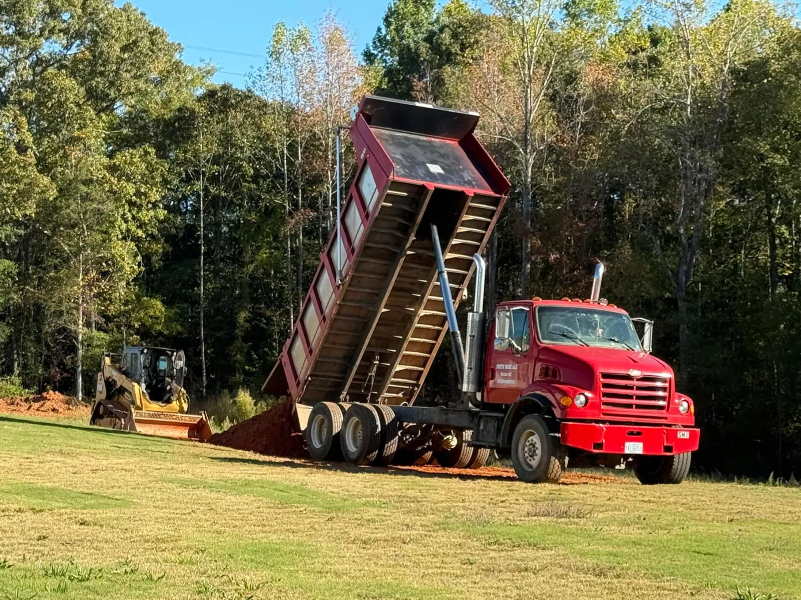 Smith Mine dump truck bed fully raised dumping red fill dirt while Cat track loader spreads it
