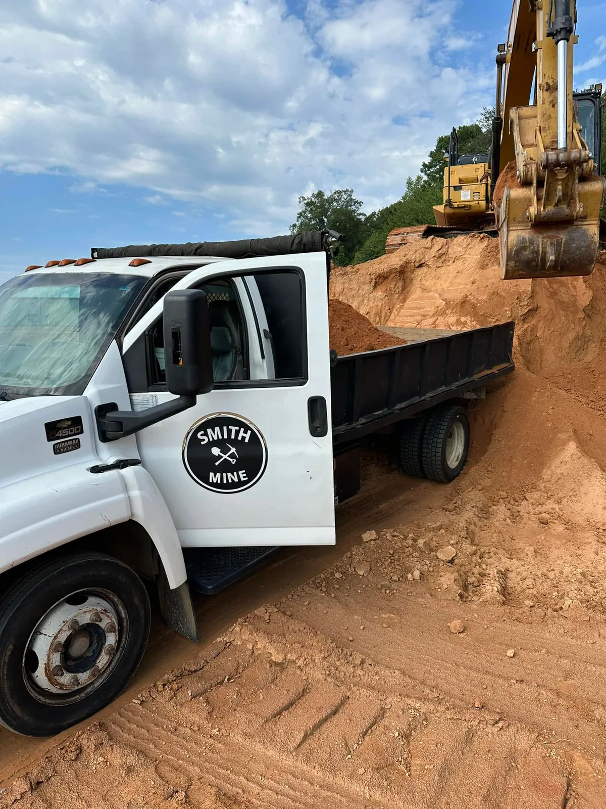 Cat excavator loading Smith Mine Chevy C4500 dump truck with fill dirt at sandy pit bank