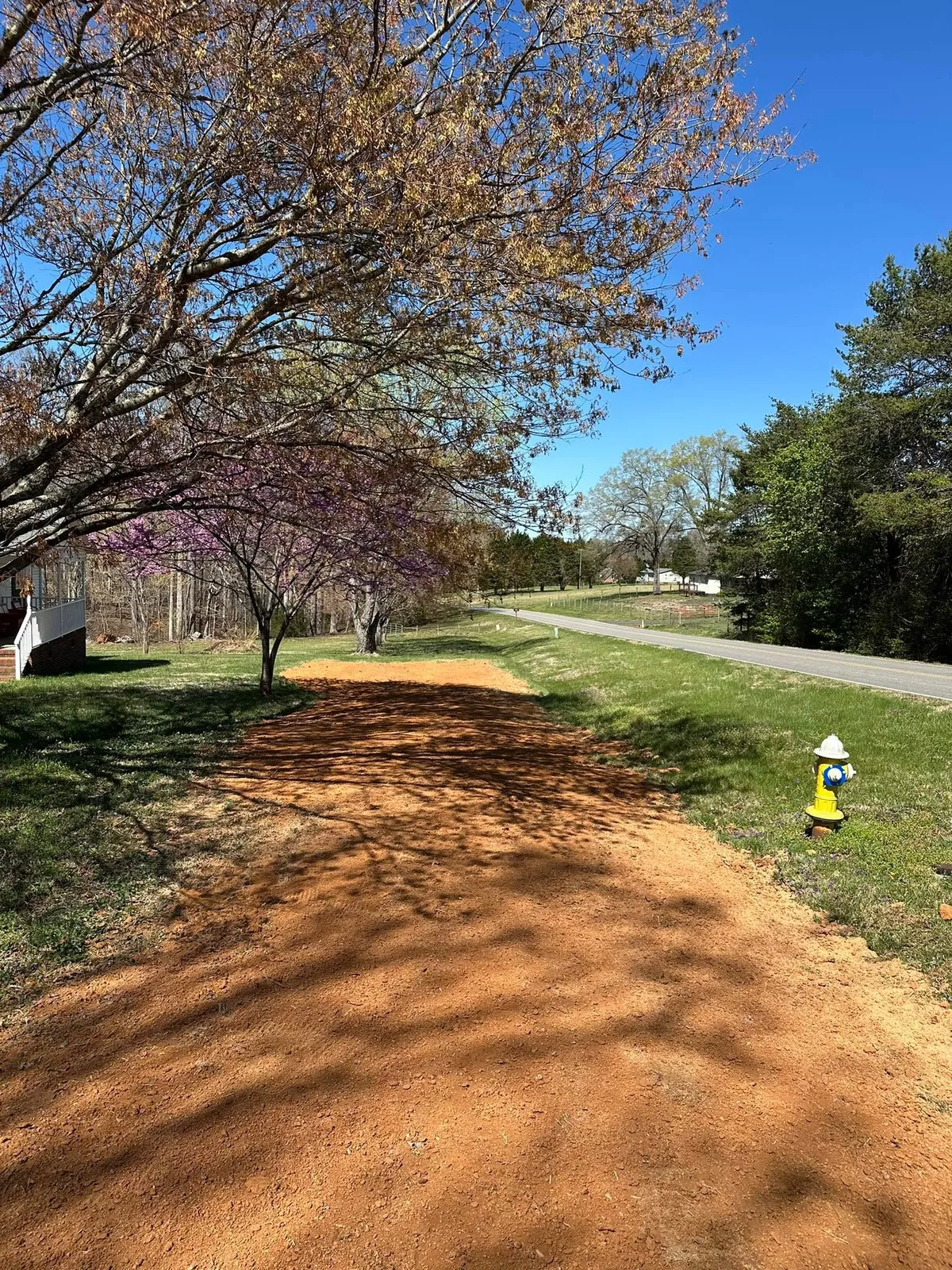 Red clay fill spread and graded smooth along roadside lawn near yellow fire hydrant, before straw