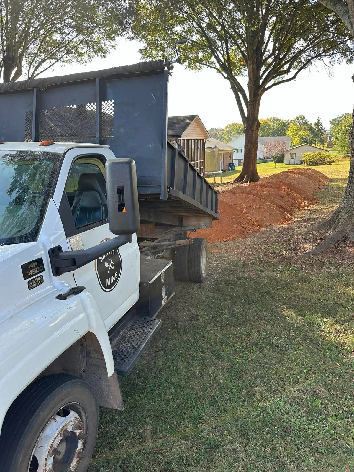 Smith Mine Chevy C4500 dumping red clay fill in a windrow across residential yard under large oak