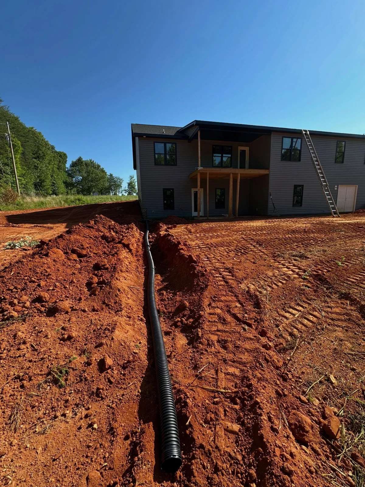 Black corrugated foundation drain pipe in trench leading away from new two-story house, red clay in Sherrills Ford, NC