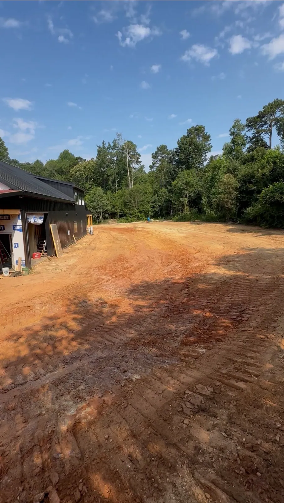 Freshly dozer-graded red clay yard beside black metal barndominium, smooth track-packed surface