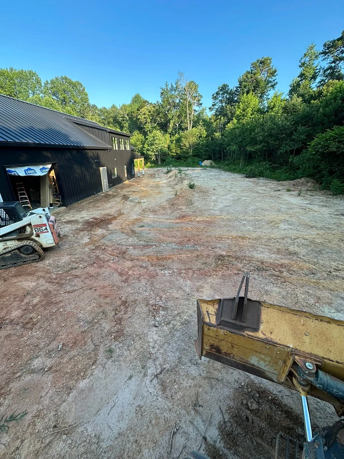 Rough uneven site beside black barndominium before dozer grading, Bobcat 864 track loader parked