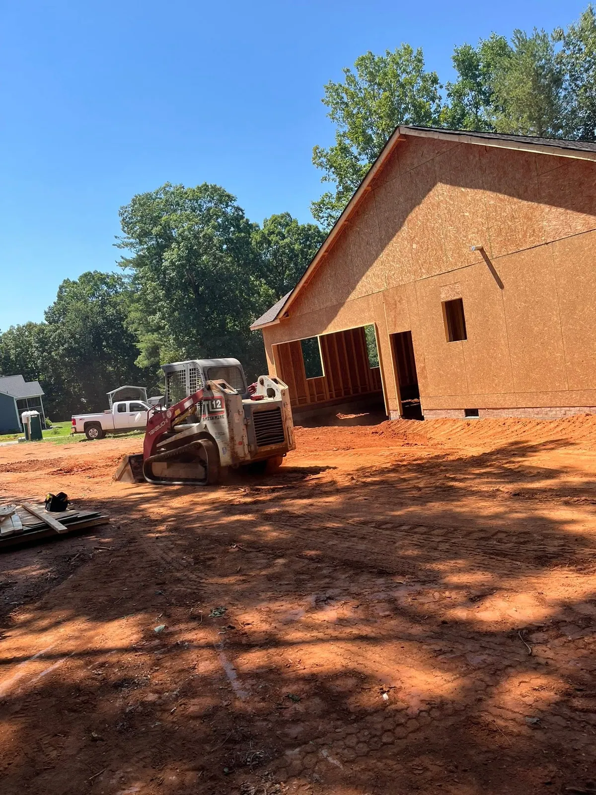 Takeuchi TL12 track loader rough-grading red clay around newly framed OSB house and garage