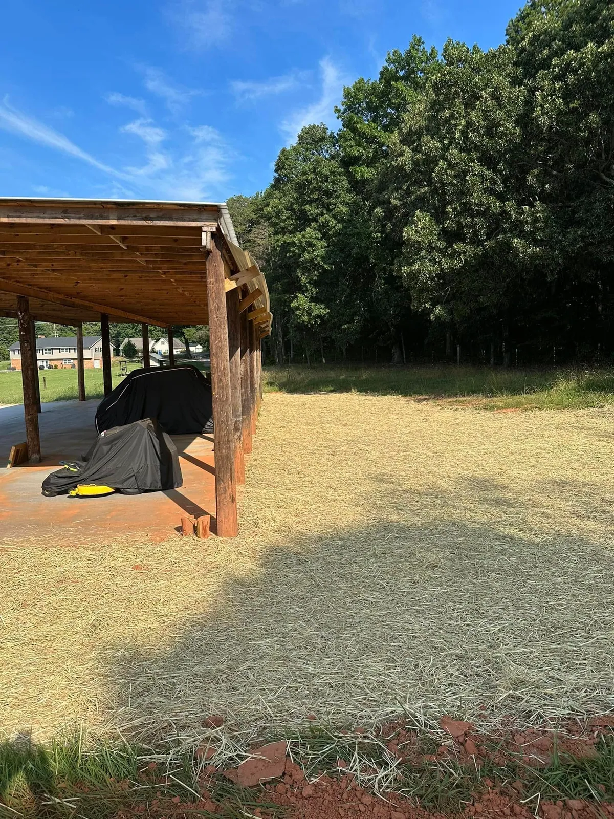 Straw-covered seeded ground beside pole shed after grading, covered vehicles under roof