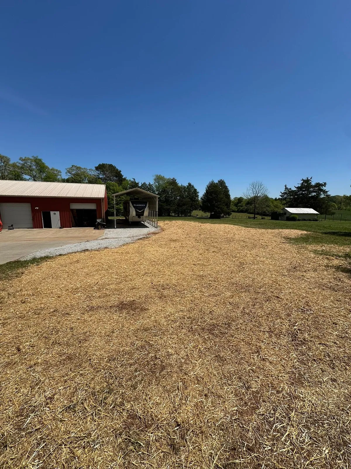 Finished graded yard seeded and strawed beside red metal shop and RV carport