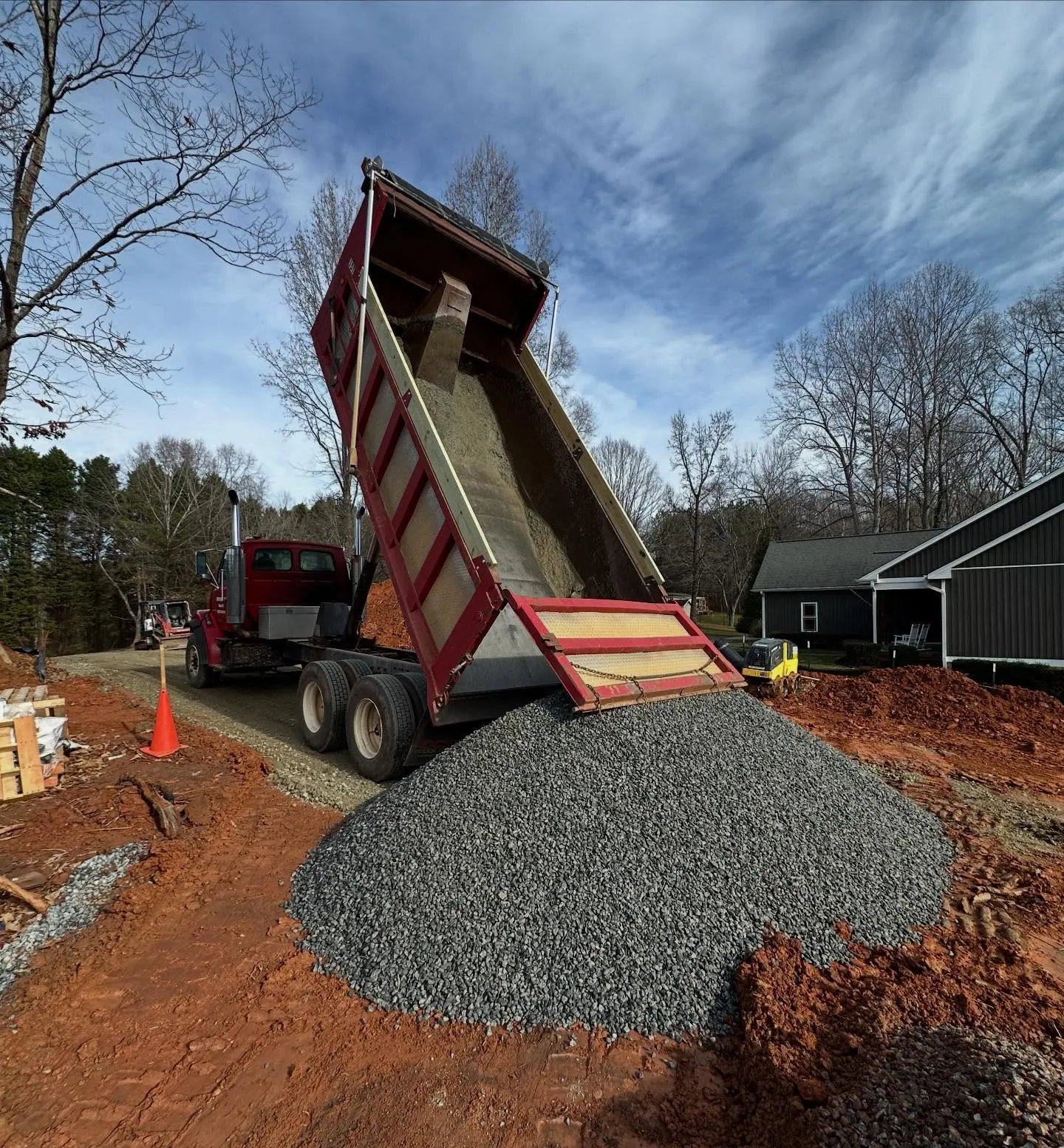 Smith Mine dump truck with bed raised dumping gray gravel pile beside dark-sided house