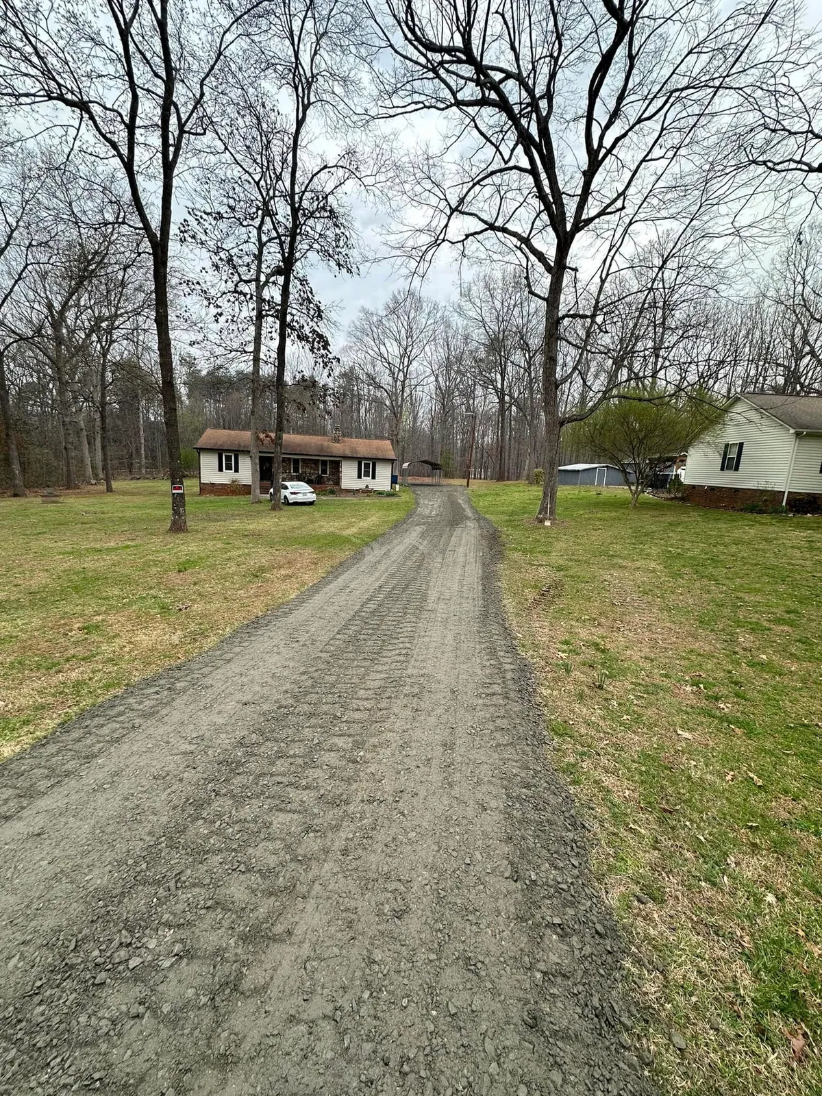 After shot: fresh crusher run gravel driveway graded past white ranch house to carport, track marks