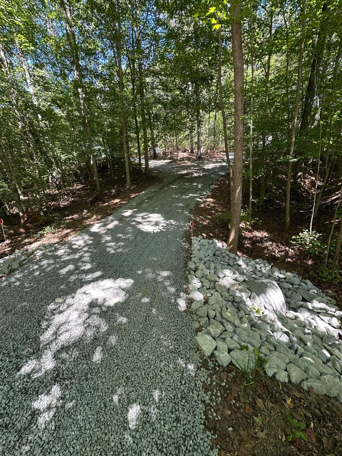 Completed gravel driveway through hardwoods with culvert end wrapped in rip-rap