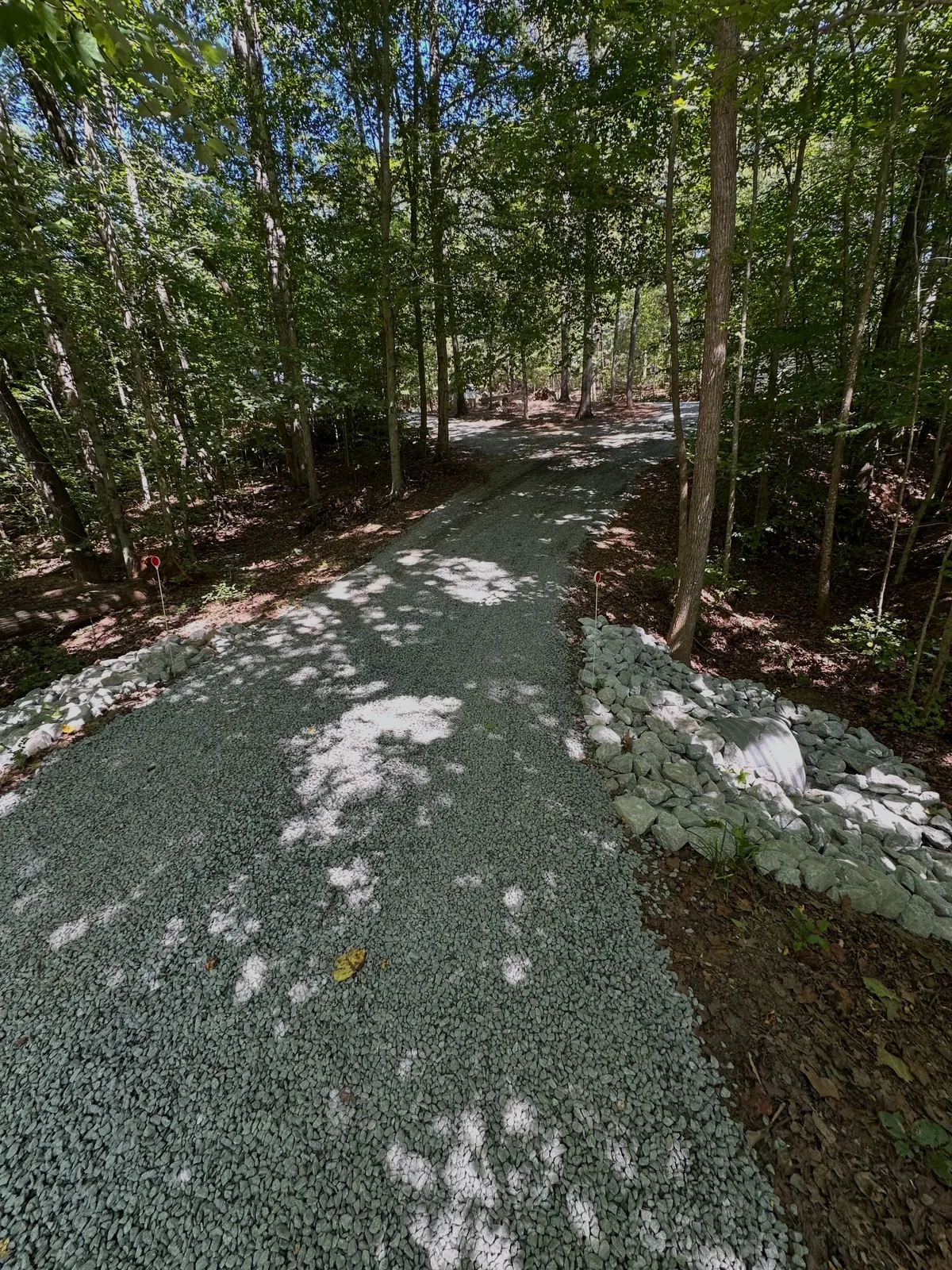 New gravel driveway through hardwoods with culvert pipe and rip-rap headwall at entrance