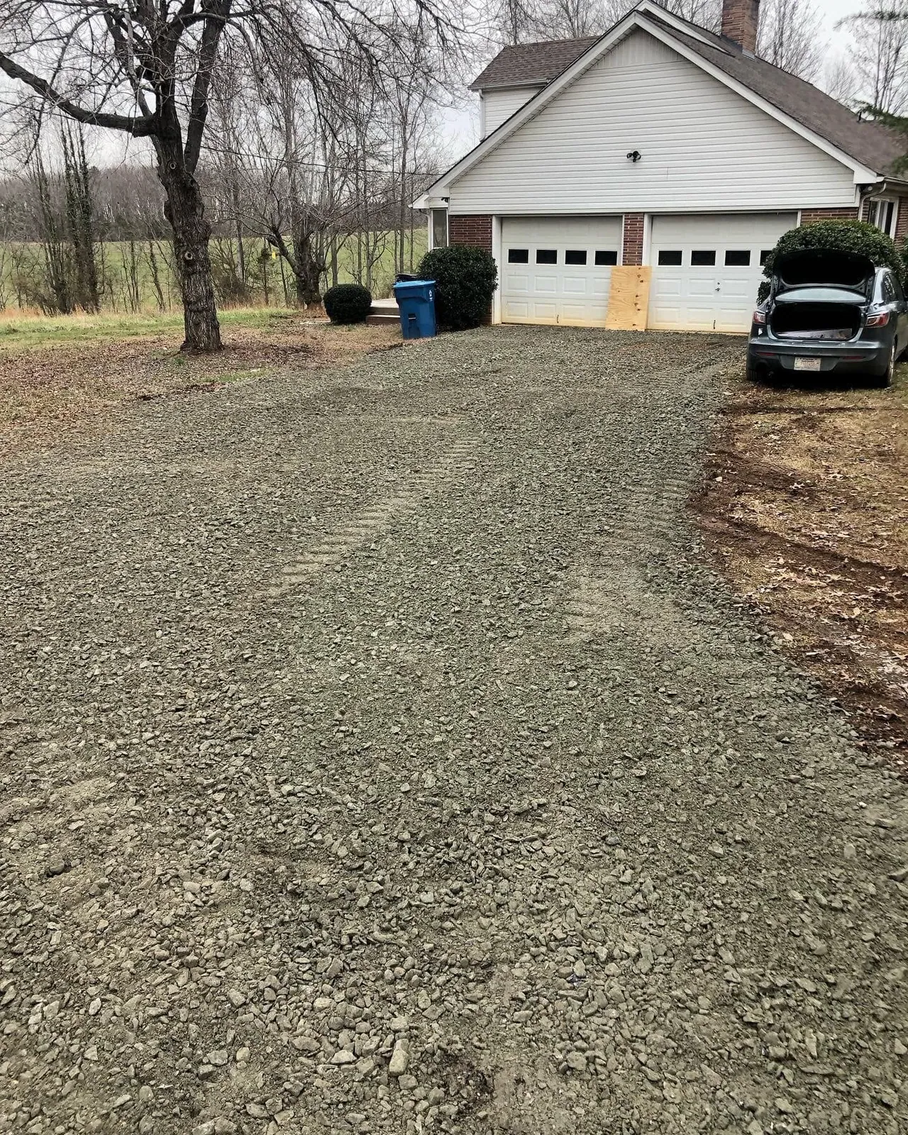 Fresh crusher-run gravel spread across driveway in front of white two-car garage, winter overcast