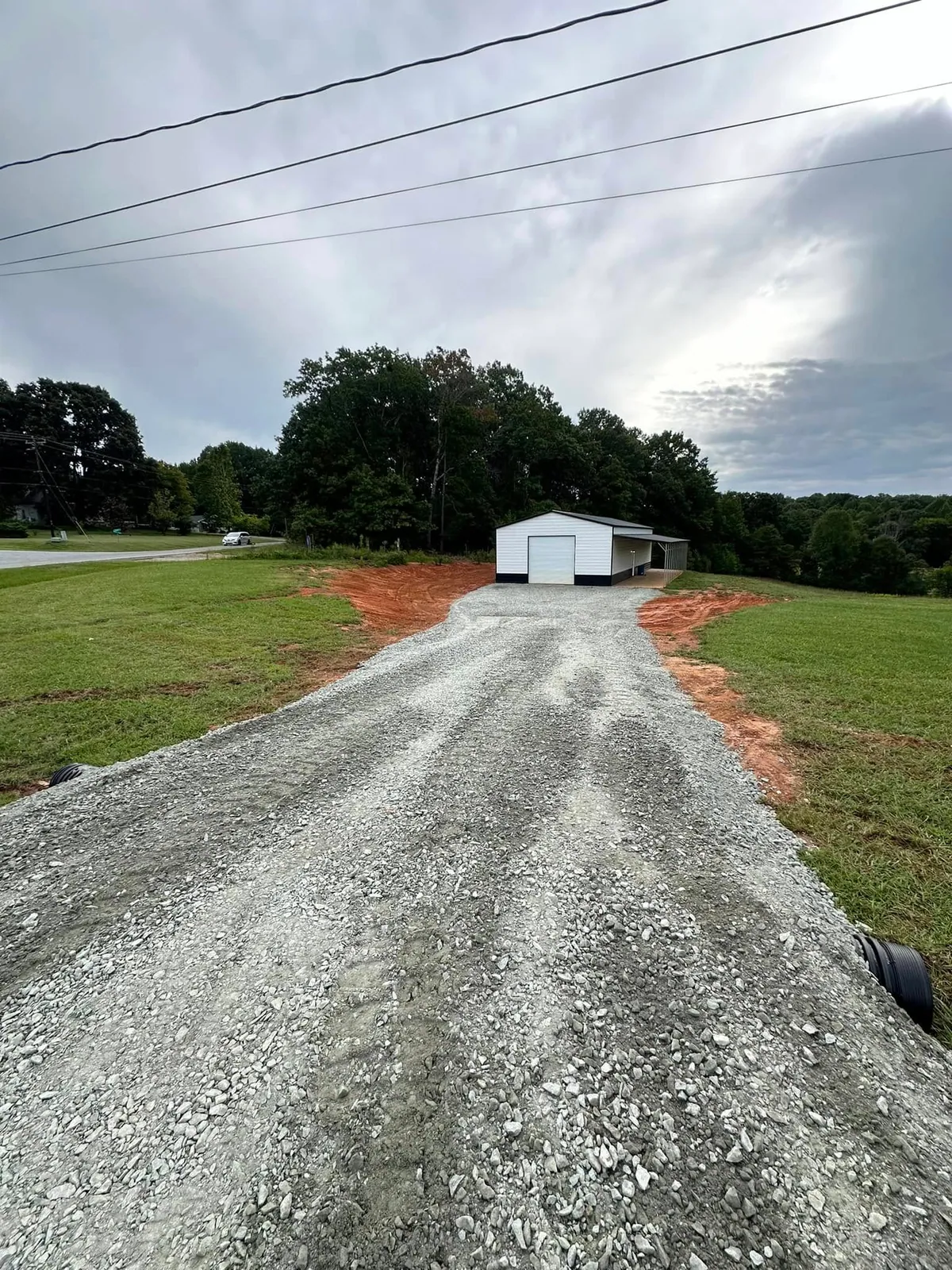 Finished gravel driveway to white metal garage with lean-to, culvert pipe ends at road ditch