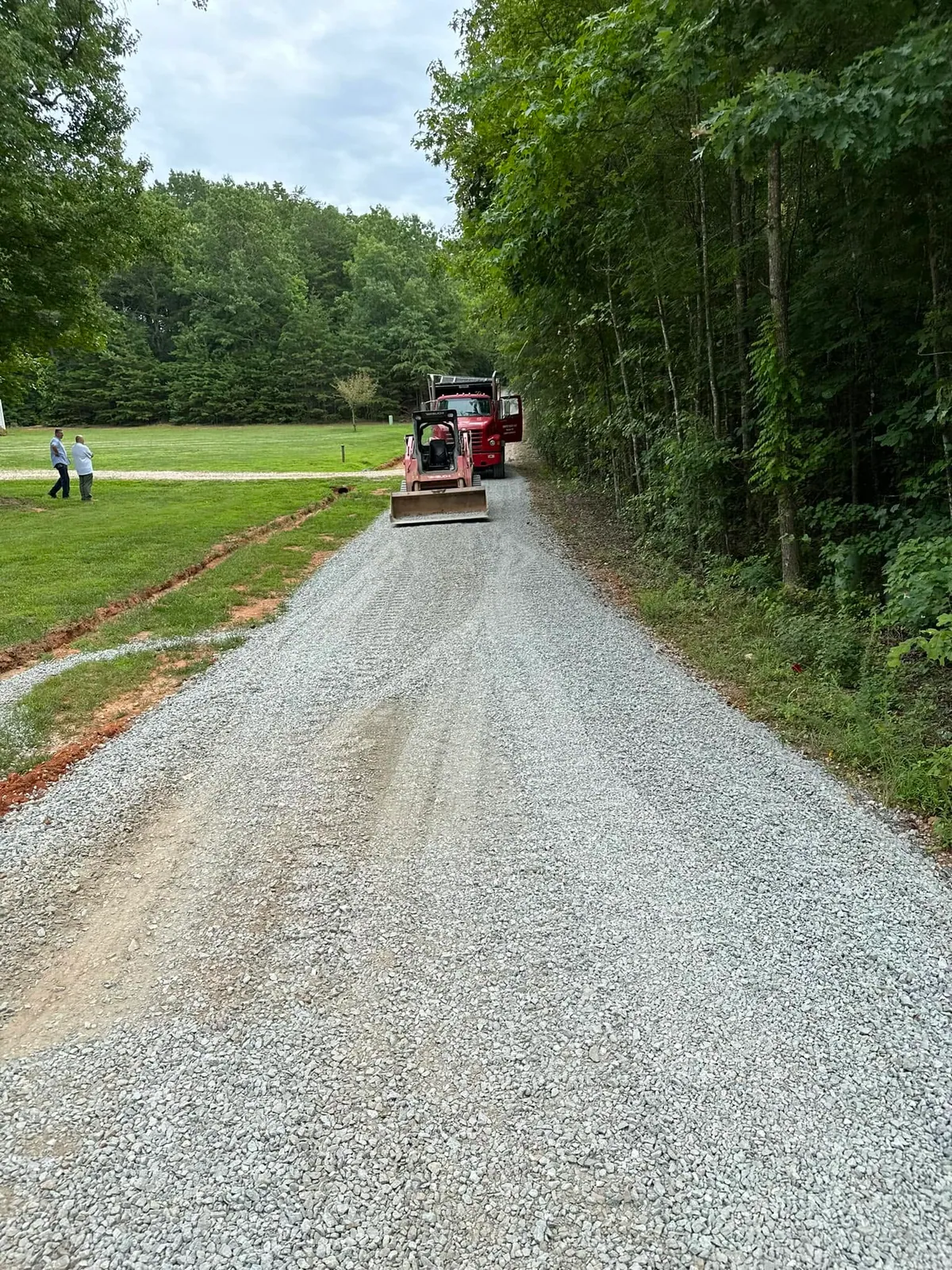 Long fresh white gravel driveway with red Takeuchi track loader and red tandem dump truck at far end