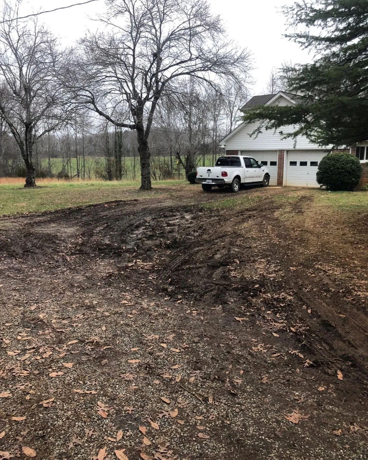 Muddy, rutted driveway in front of white two-car garage with white Ford F-150, before gravel