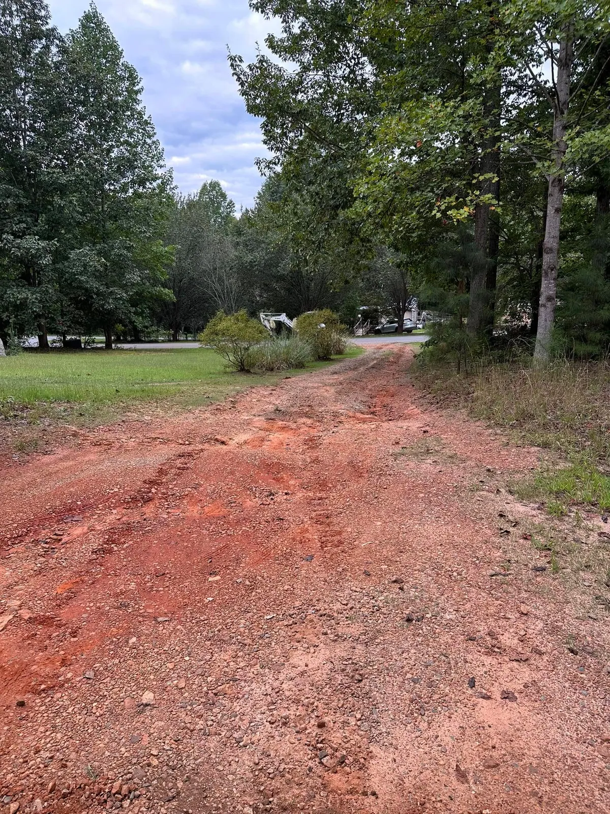 Rutted, washed-out red clay gravel driveway through woods toward road before regrading