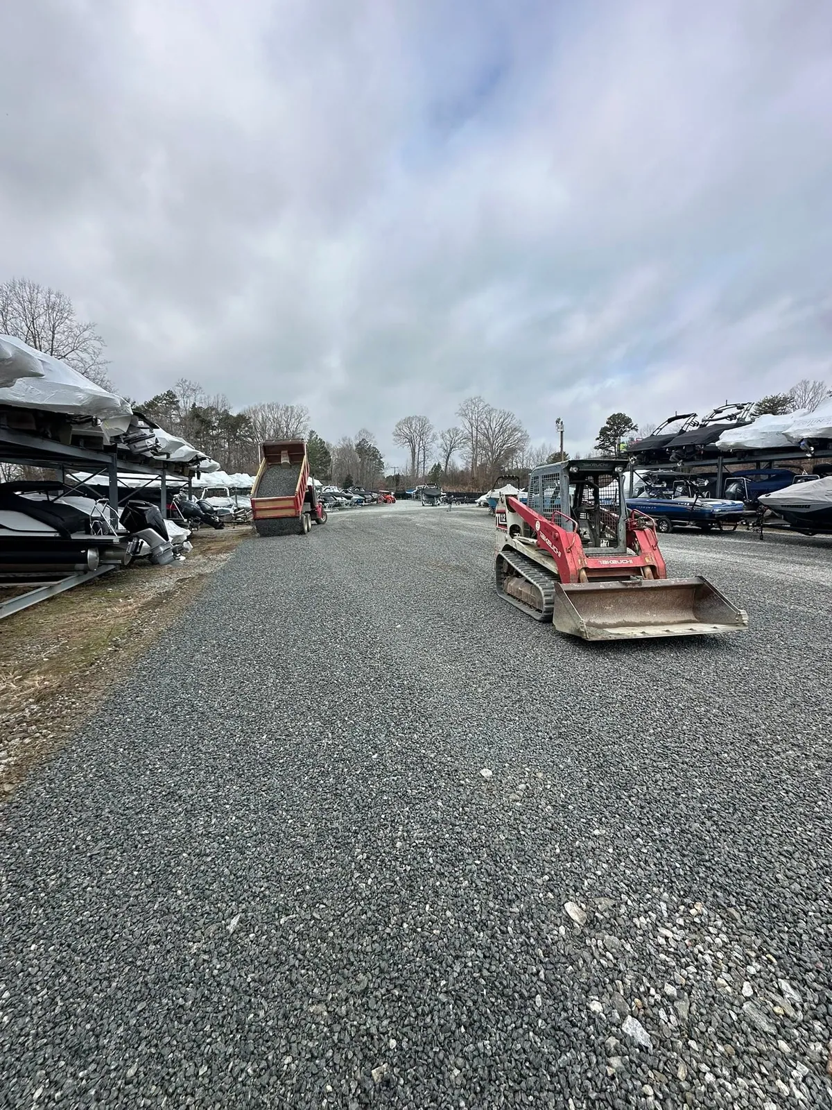 New gray gravel lane between marina boat racks, TL12 loader and dump truck dumping at end