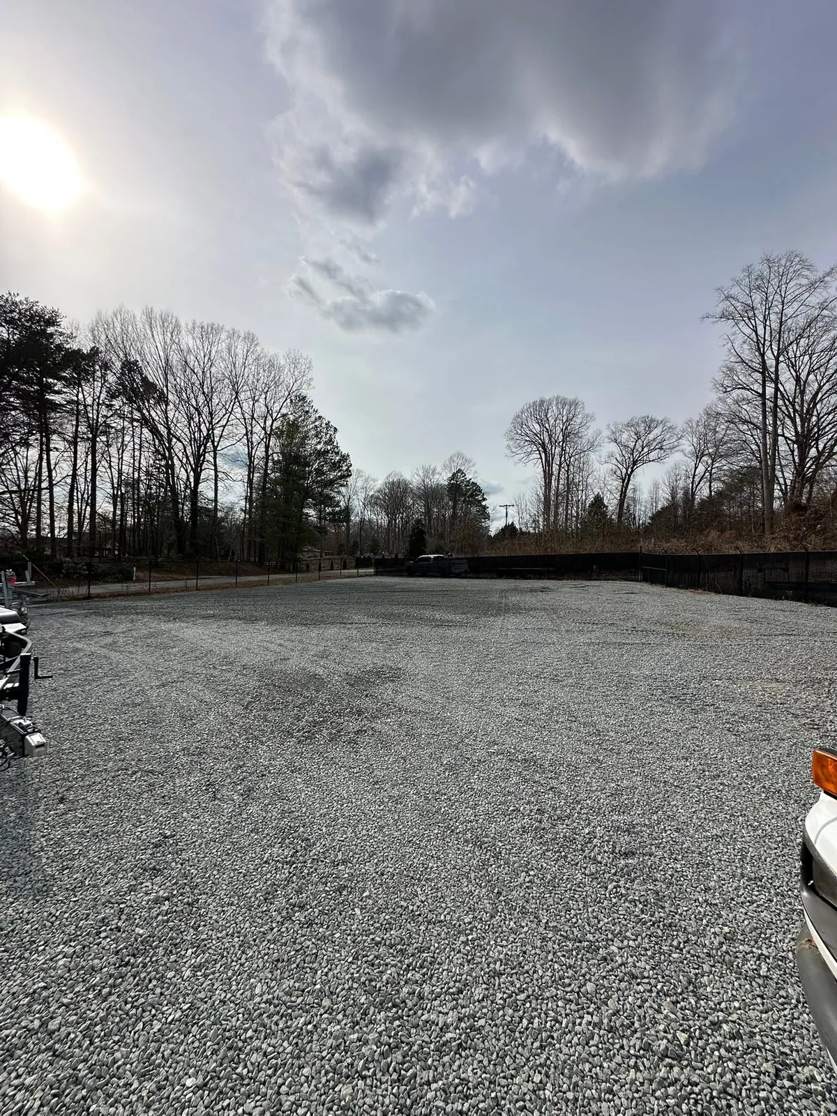 Completed wide gravel parking lot enclosed by black chain-link fence, boat trailers at edge