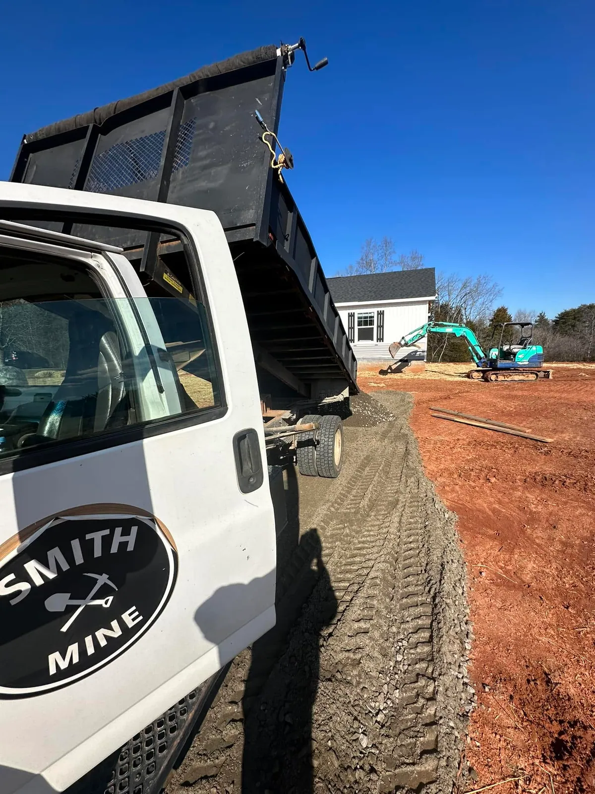 White Smith Mine dump truck tailgating crusher run gravel strip; teal mini excavator by new white cottage