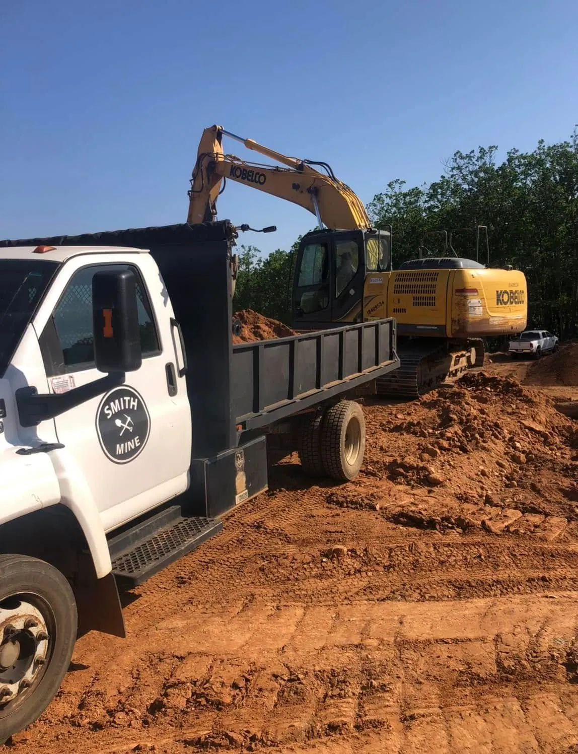 Smith Mine white Kodiak dump truck being loaded by yellow Kobelco excavator on a red clay cut