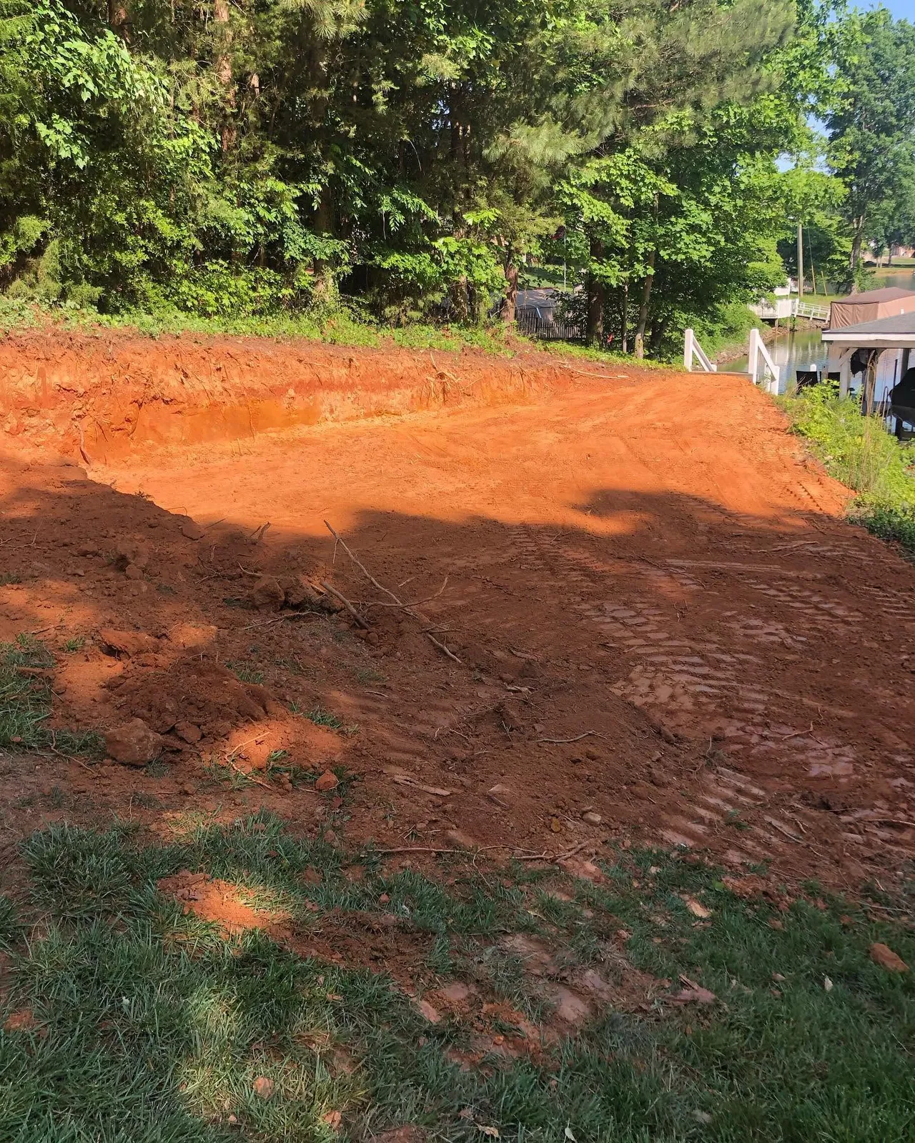 Red clay bench cut into lakefront slope, vertical cut face, dock and boathouse visible