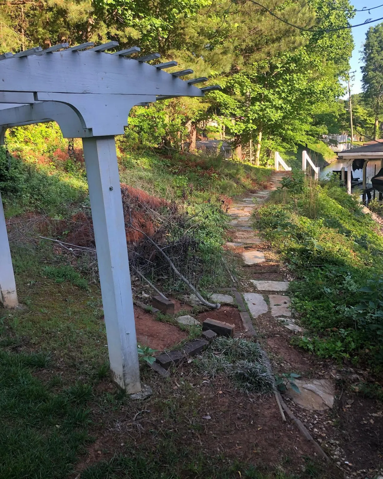 Before shot: overgrown lakefront yard with pergola, weedy flagstone path down to dock