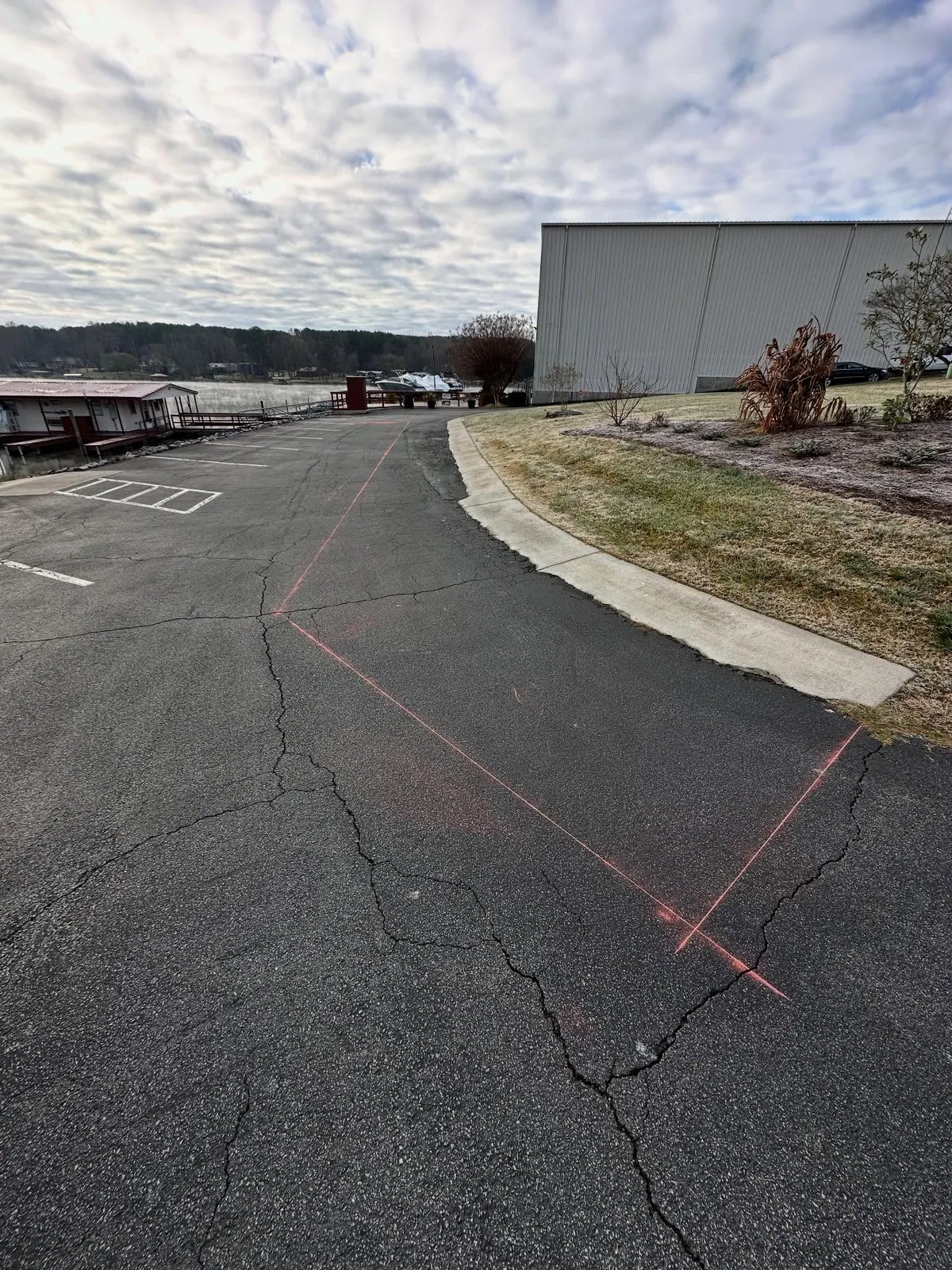 Cracked marina asphalt drive with pink paint marking section to be cut out along curb