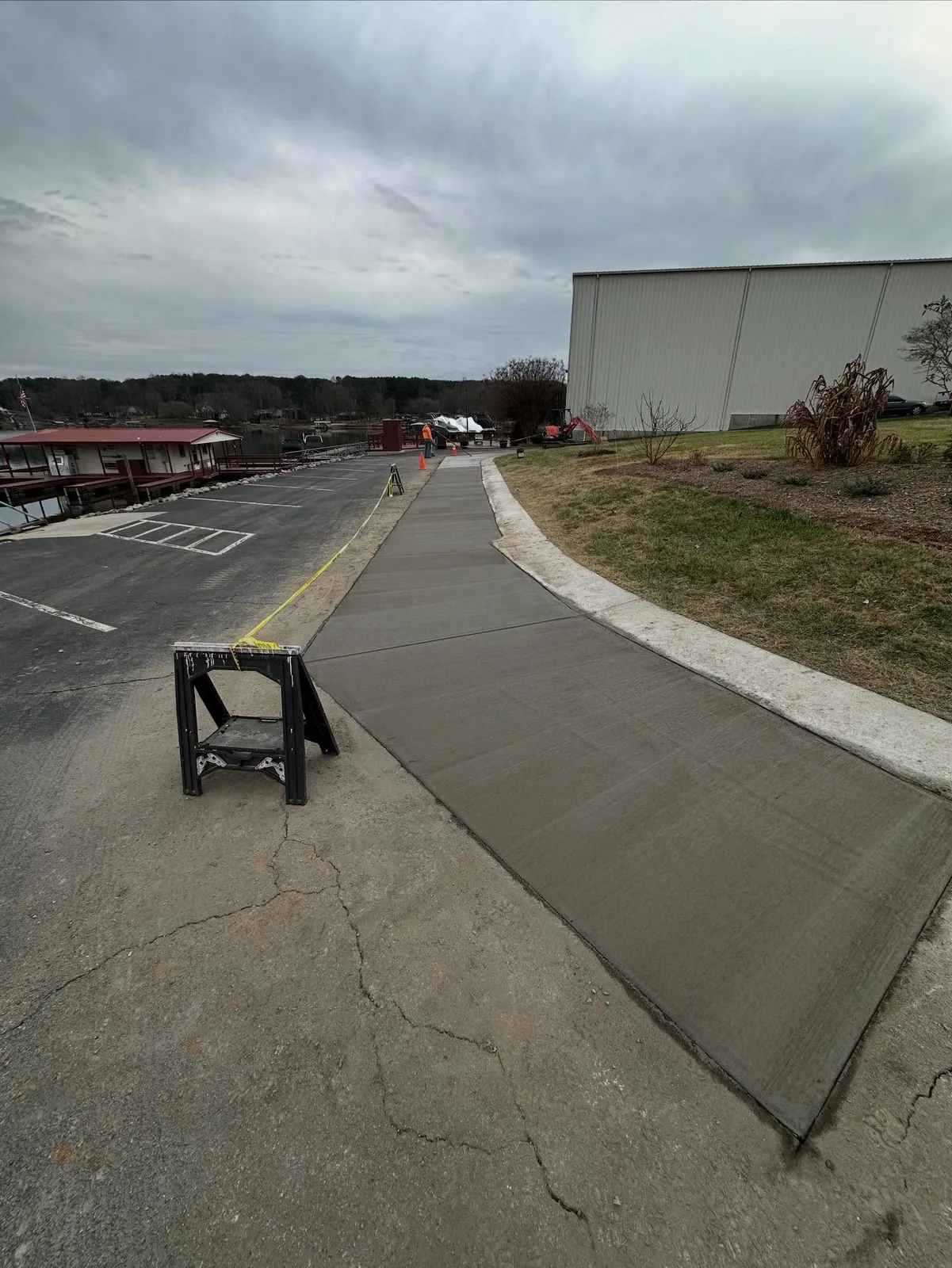Fresh concrete walkway poured along marina curb replacing cut asphalt, caution tape and sawhorse