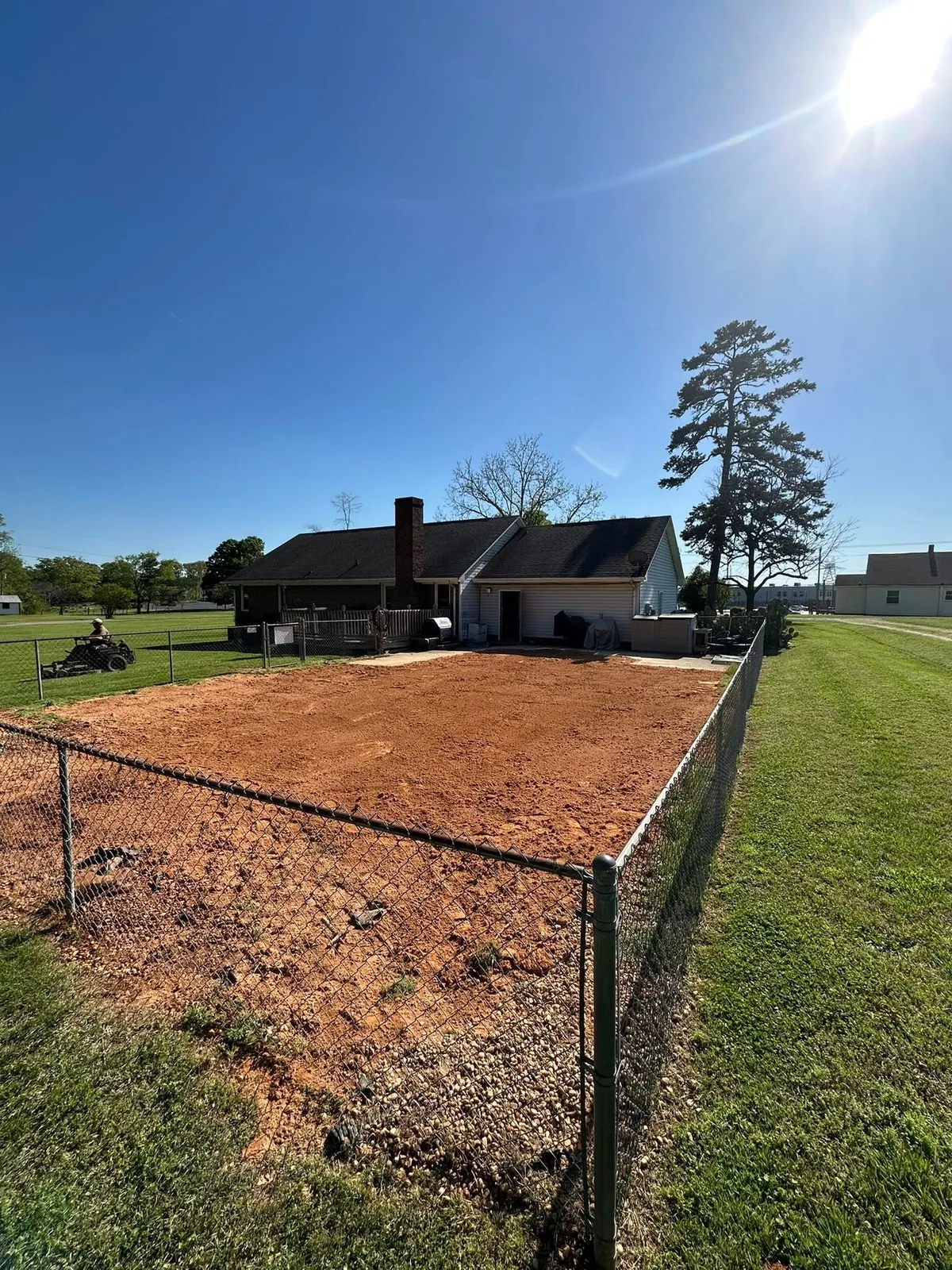 Fenced backyard filled and graded flat with red clay where pool was removed, house behind