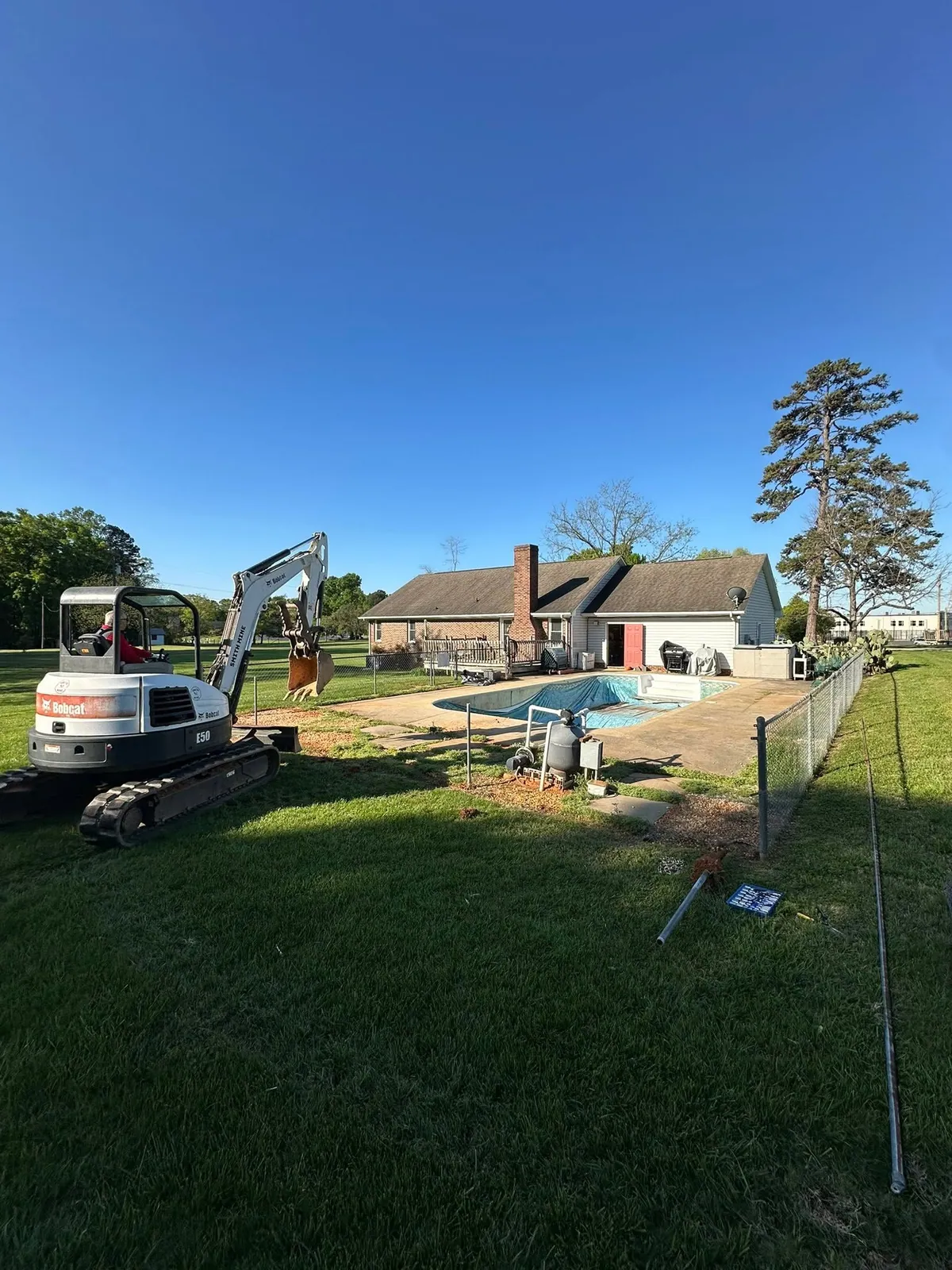 Bobcat E50 mini excavator on lawn beside covered in-ground pool, staged to fill the pool in