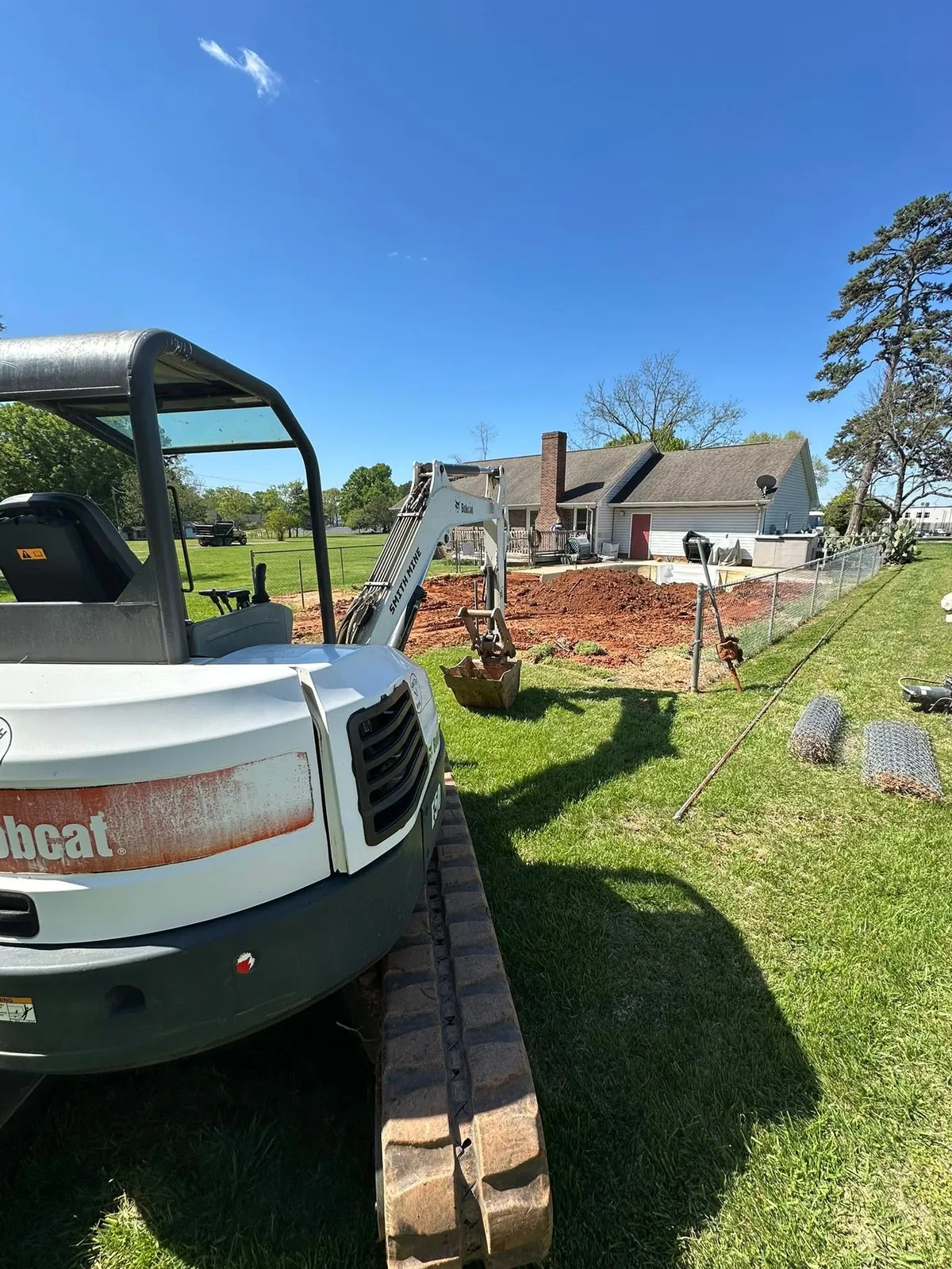 Bobcat E50 mini excavator with Smith Mine decal filling backyard pool pit with red clay, fence rolled back