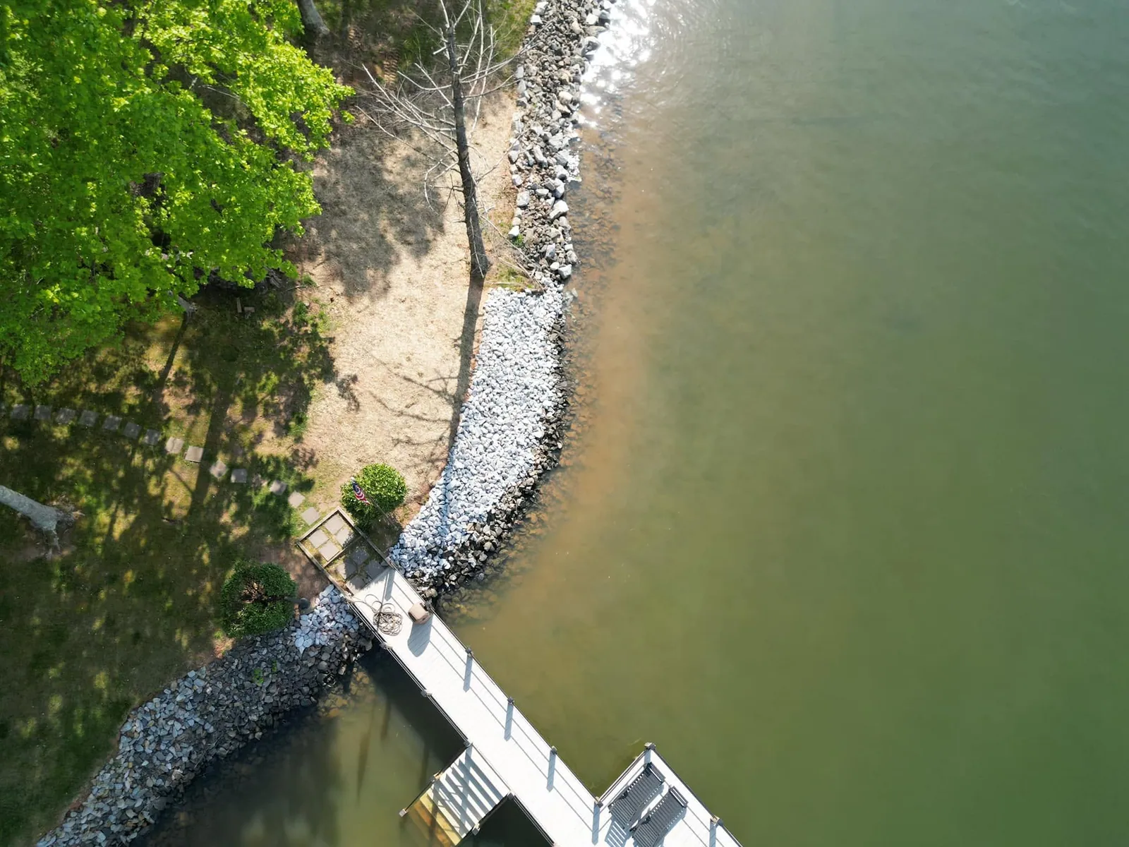 Drone aerial of finished rip-rap shoreline curving around lake lot, new light rock, dock and stepping stones