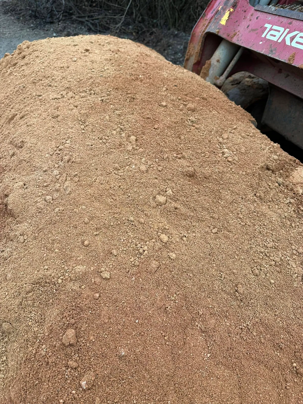 Close-up of tan screened sand pile with red Takeuchi track loader behind it