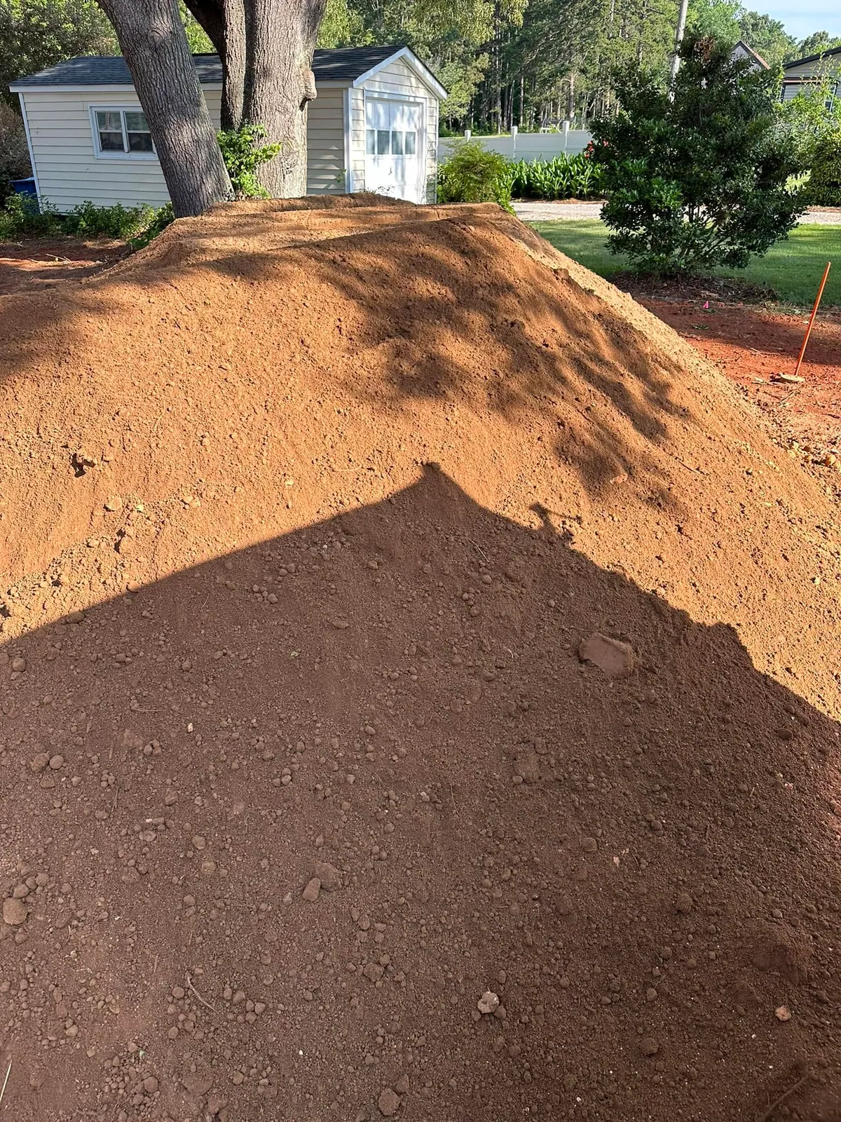 Large pile of fine brown screened topsoil dumped in backyard beside detached garage and vinyl fence
