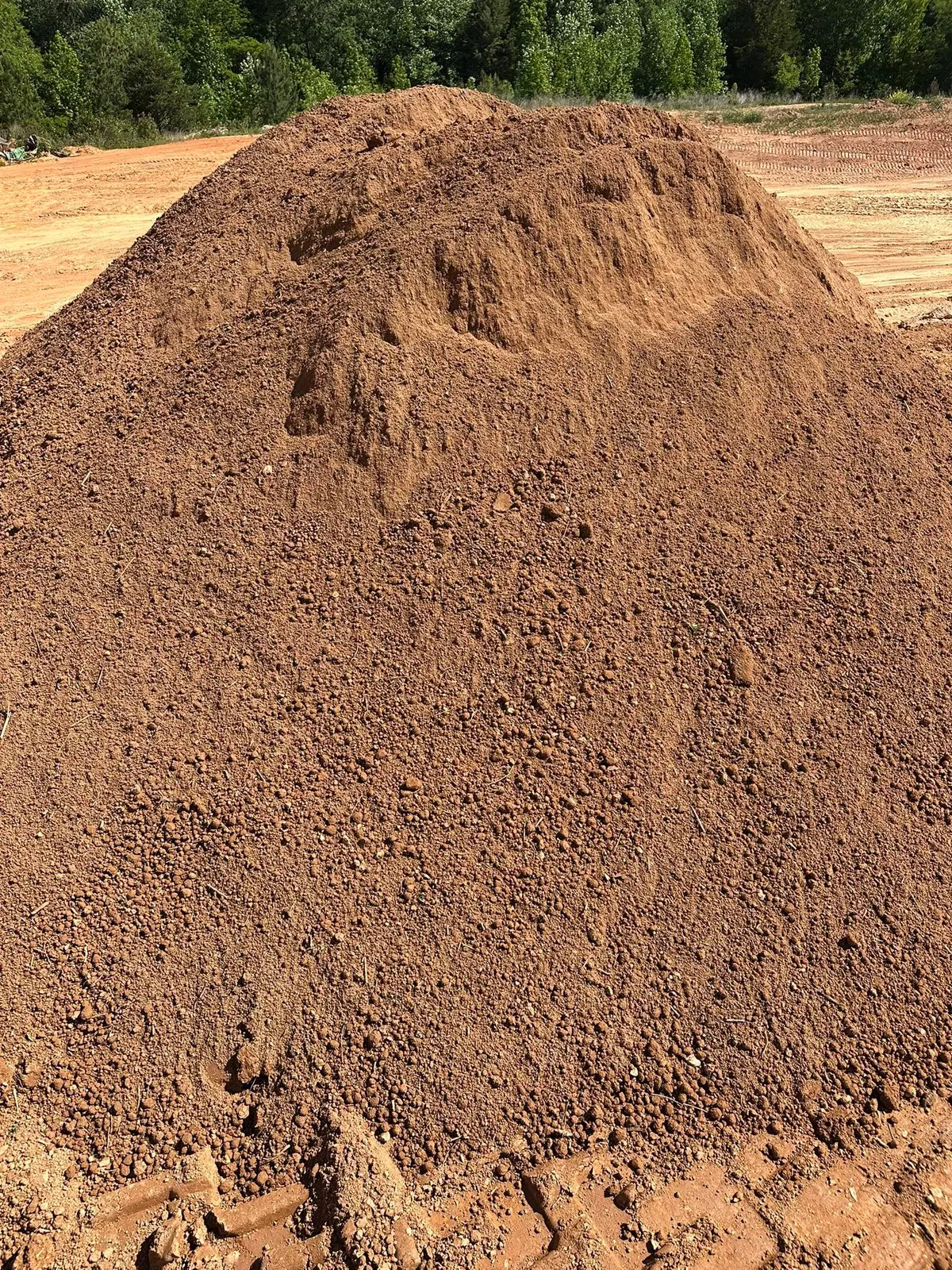 Large stockpile of screened topsoil on graded site, pit and treeline behind in Catawba, NC