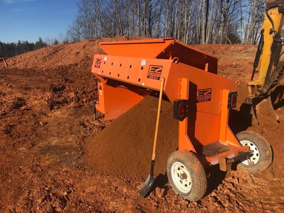 EZ Screen 600 screener being fed by excavator bucket, screened topsoil piling under it