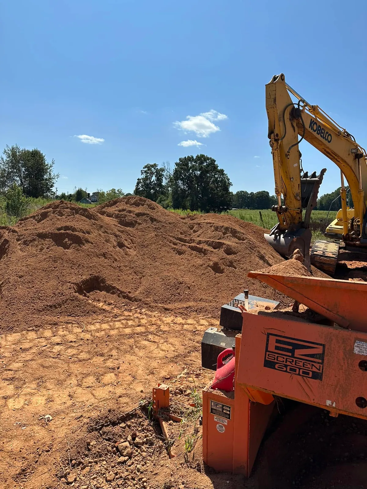 Kobelco excavator feeding EZ Screen 600 portable screener beside large pile of screened fill